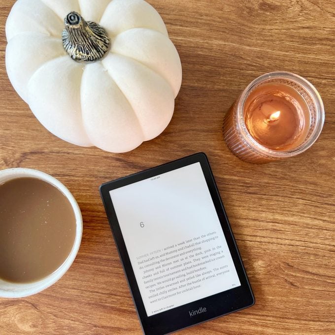 Kindle Paperwhite sobre una mesa con una vela, una mini calabaza blanca y una taza de café, visto desde arriba