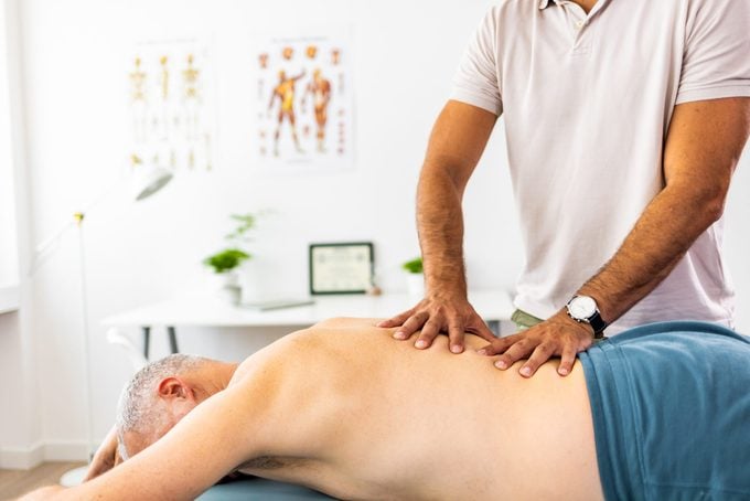 Una foto de un hombre maduro acostado boca abajo y recibiendo un masaje en la espalda por parte de un fisioterapeuta en una clínica