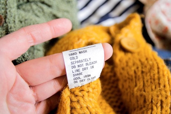 primer plano de una mano mirando las instrucciones de lavado en una etiqueta de cuidado en una manta de lana