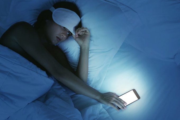 Mujer acostada en la cama y mirando el teléfono inteligente por la noche