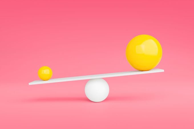 dos esferas amarillas en cada extremo de una balanza sobre fondo rosa;  la bola más pequeña es la bola más pesada