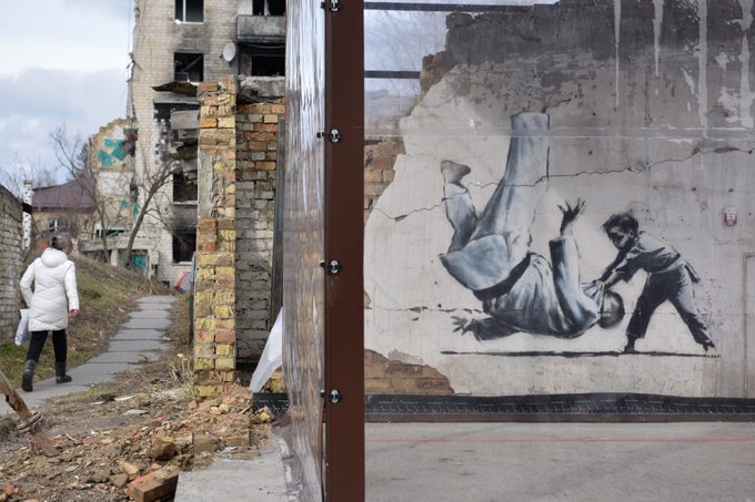 Una mujer camina cerca del graffiti del artista Banksy...