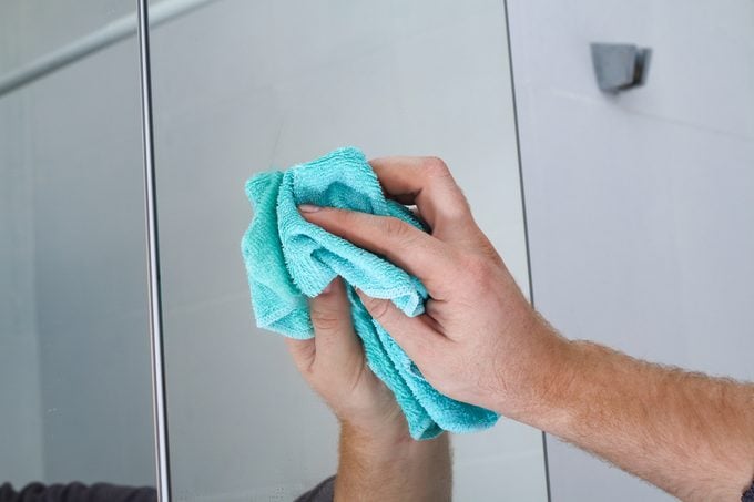 Un hombre limpia un armario con espejo en el baño con un trapo.  Limpieza de la casa, baño.