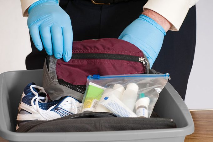 Manos enguantadas de la persona de seguridad del aeropuerto examina el contenido de la papelera y las pertenencias de un viajero