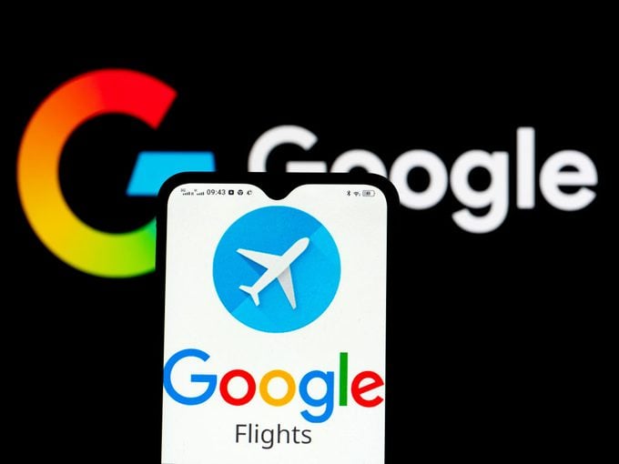 Logotipo de Google Vuelos mostrado en un teléfono inteligente frente al logotipo de Google