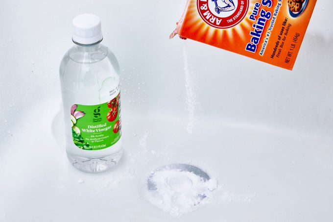 verter bicarbonato de sodio en el desagüe de una bañera, una botella de vinagre blanco cerca