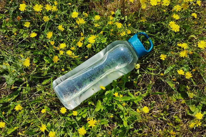 Drinking bottle lying in the grass with some yellow flowers